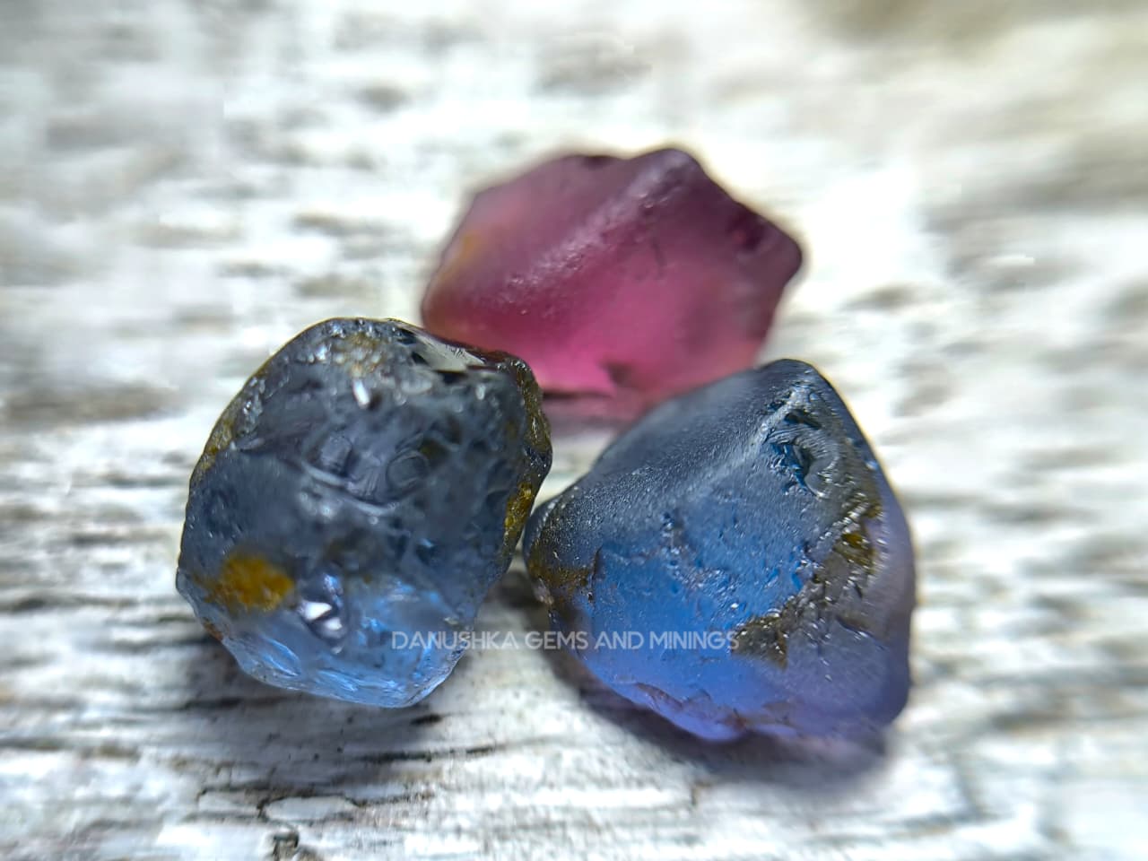 Three-piece facet-grade Spinel rough parcel with color-change, purplish pink, and blue Spinel stones showing natural inclusions and cutting potential.